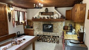 A cozy kitchen with a stone fireplace, wooden cabinets, and a dining area with a table set for two. - Villa White Stone - Zlatograd (Zlatograd)
