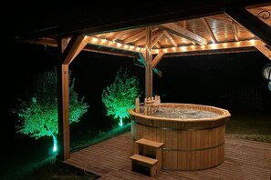 Ein hölzernes Whirlpool unter einem Pavillon, mit Stufen, die zu ihm führen, umgeben von einer Terrasse.