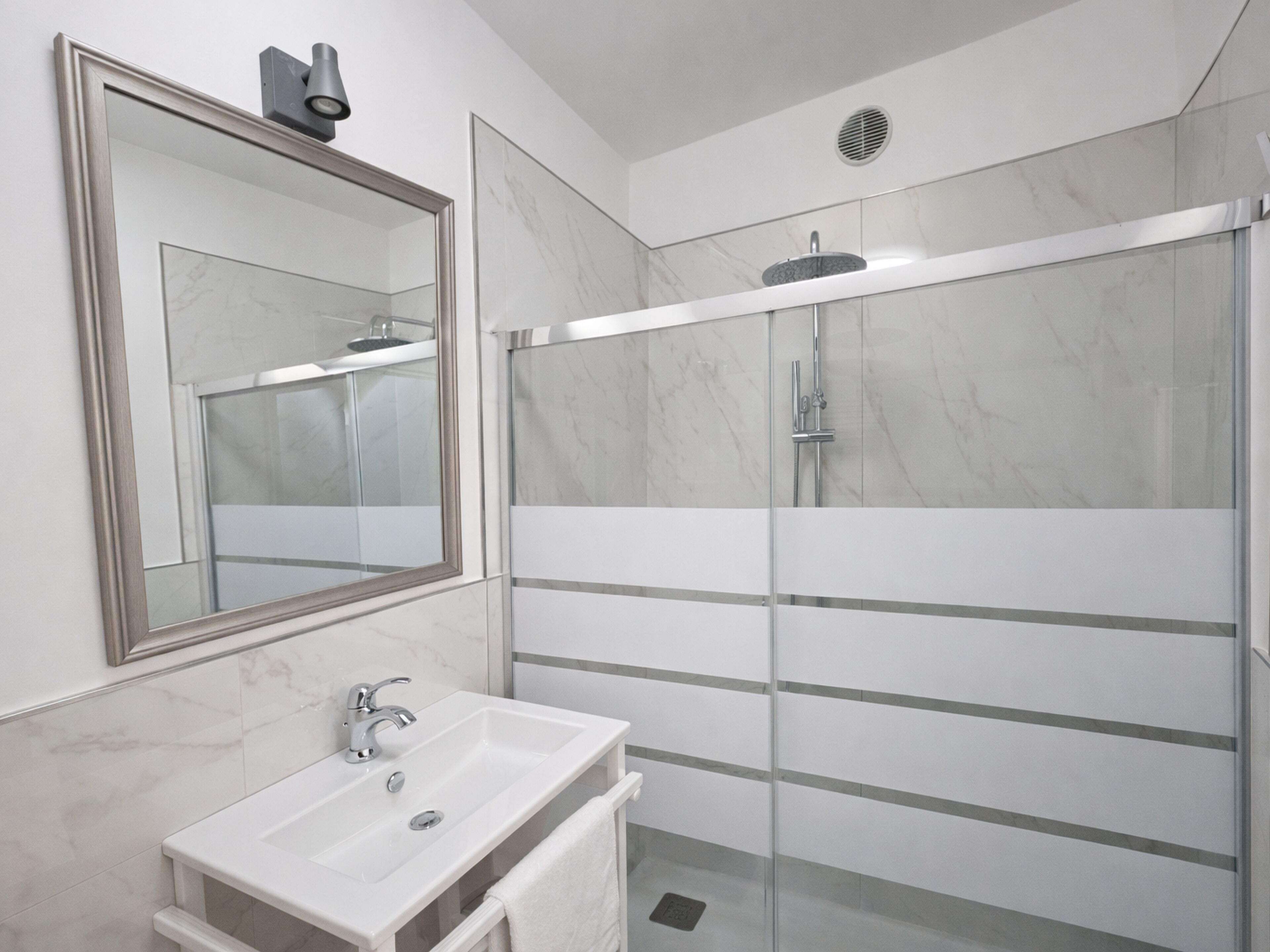 Un baño moderno con un espejo grande, un lavabo y una zona de ducha con mampara de cristal.