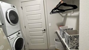 Une buanderie équipée de machines à laver et de sèche-linge superposés, d’une porte, d’un étendoir et d’une poubelle.