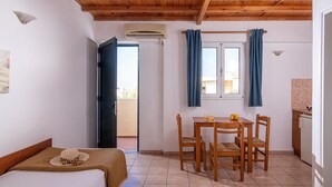 A room with a bed, a table with chairs, a window with curtains, an air conditioning unit, and a view of the outside. - Spacious Apartment with Sea View & Shared Pool (Hersonissos)
