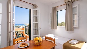 A room with a balcony, a table with a plate of croissants and a fruit basket, a bed with a brown towel, and a window with curtains. - Spacious Apartment with Sea View & Shared Pool (Hersonissos)
