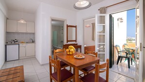 A modern kitchen with white cabinets, a dining table with chairs, and a view of the outdoors through an open door. - Spacious Apartment with Sea View & Shared Pool (Hersonissos)