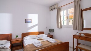 Ein Hotelzimmer mit einem hölzernen Bett, einem Schreibtisch, einem Sessel, einem Nachttisch, einer Topfpflanze und einem fenster mit Vorhängen.
