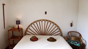 A room with a bed, a rattan chair, a small table with a lamp, and a wall-mounted light fixture. - THE SWEET VILLA - A charming place of Mediterranean quiet. (Santa Maria di Castellabate)