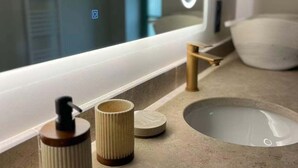 Un meuble-lavabo pour la salle de bain, avec un miroir, un distributeur de savon, un porte-brosse à dents et un petit lavabo.