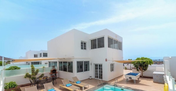 A modern two-story building with a pool, outdoor seating, and a clear view of the sea.