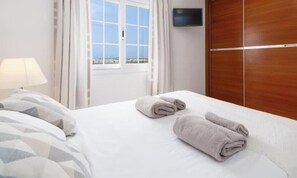 Une chambre d’hôtel avec un lit, un téléviseur fixé au mur et une fenêtre avec des rideaux.