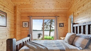 Une chambre dans une cabane en bois, avec un lit, une vue sur un lac et un quai.