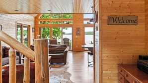 L’intérieur d’un chalet en bois, avec un escalier, un canapé, une table et une pancarte « Bienvenue ».