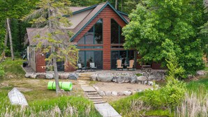 Une cabane avec un sentier en pierre menant à une terrasse, entourée de verdure et d’arbres.