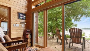 L’intérieur d’un chalet en bois, avec une grande porte-fenêtre coulissante donnant sur une terrasse extérieure d’où l’on peut admirer un lac.