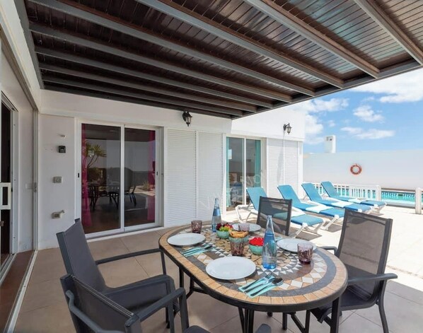 An outdoor dining area with a table set for four, surrounded by chairs, and a pool in the background.