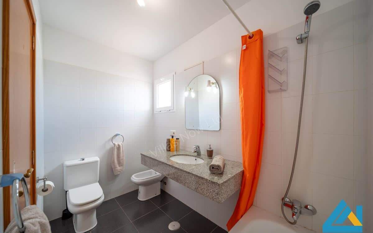 Une salle de bain équipée d’un WC, d’un bidet, d’un lavabo, d’un miroir, d’une douche et d’un rideau de douche orange.