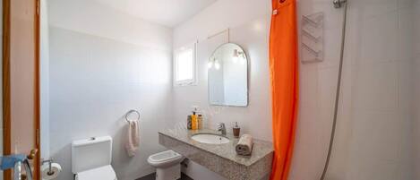 Une salle de bain équipée d’un WC, d’un bidet, d’un lavabo, d’un miroir, d’une douche et d’un rideau de douche orange.