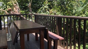 An outdoor wooden deck with a table and benches, surrounded by lush greenery and a clear blue sky. - Steps from the beach, 2-bedroom house with WiFi, AC in awesome Puako Beach (Waimea)