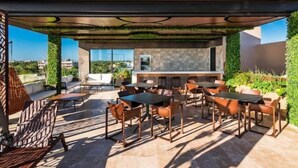 An outdoor patio with a covered seating area, a bar, and a view of the cityscape. - Tulum City Apartments M-005 (Tulum)