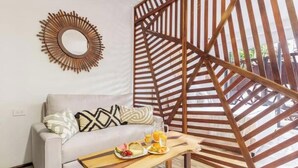 A modern living room with a sofa, a coffee table with breakfast items, a decorative mirror, and a wooden partition. - Tulum City Apartments M-005 (Tulum)