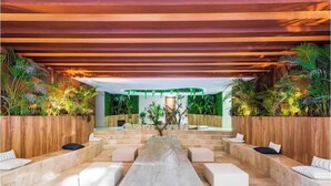 A modern indoor space with a long, central seating area, wooden walls, and tropical plants. - Tulum City Apartments M-123 (Tulum)