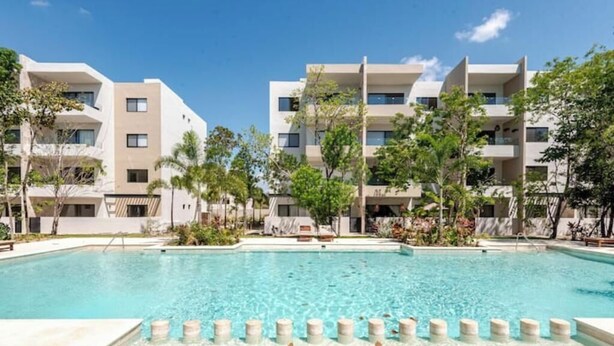 A modern hotel with a swimming pool, multiple balconies, and lush greenery.