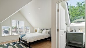 Un dormitorio con cama, ventana, escritorio y vistas al exterior.