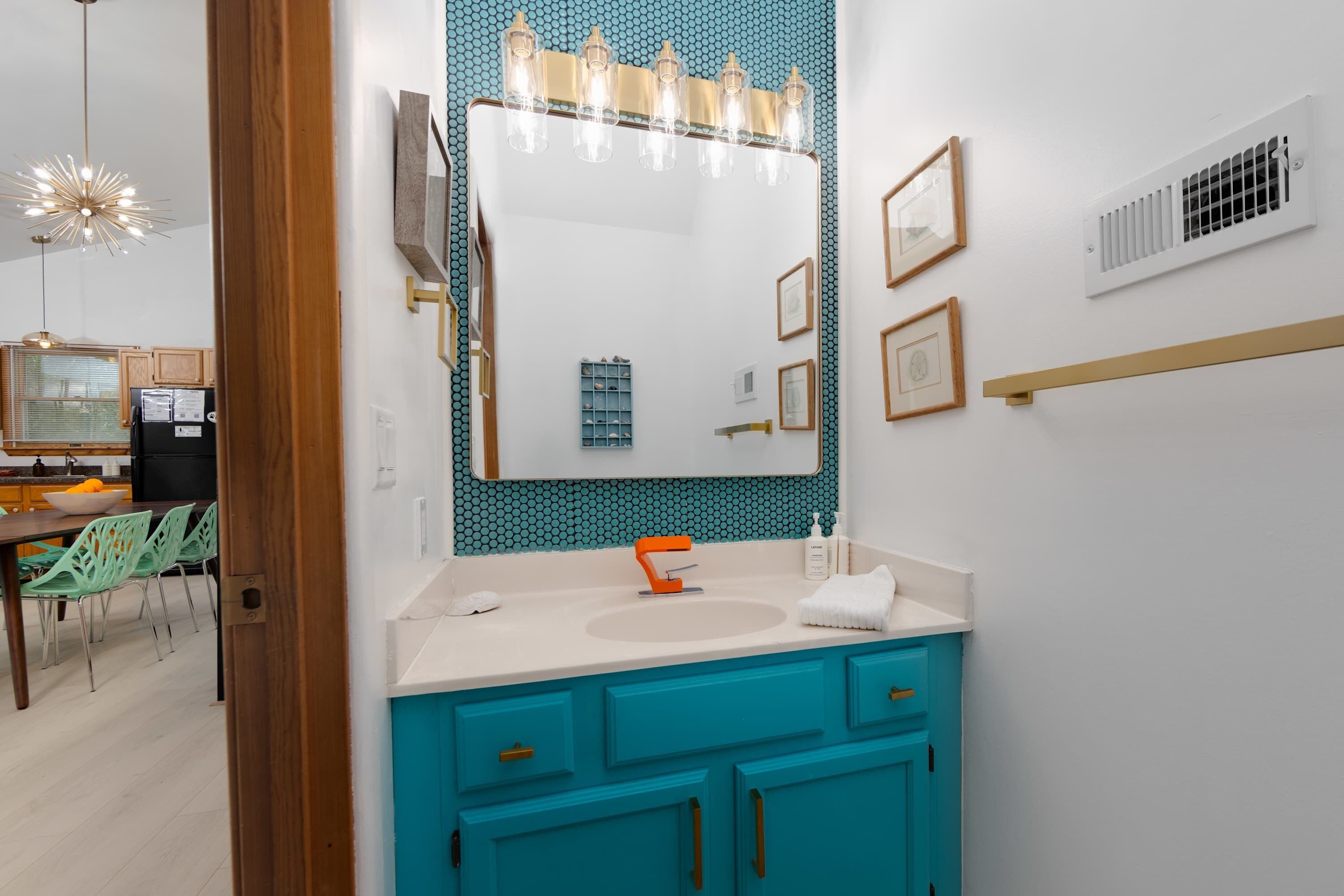 Une salle de bain avec un grand miroir, un lavabo et des meubles de couleur turquoise.