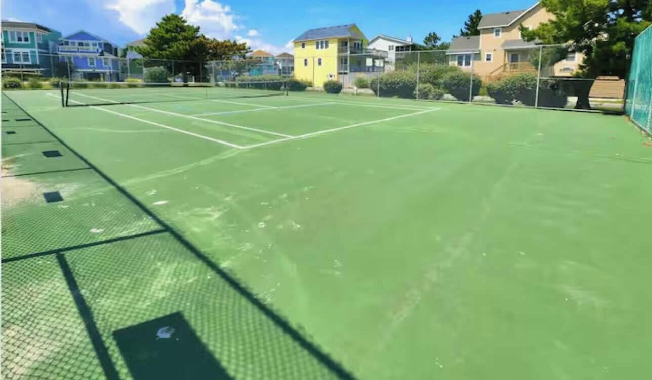 A tennis court with a net, surrounded by houses and greenery.