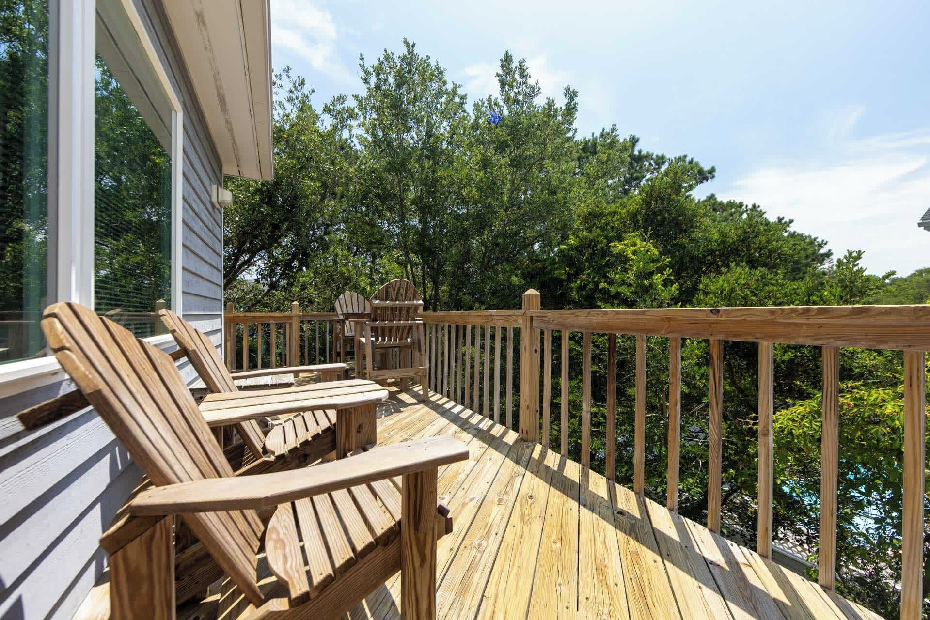 A wooden deck with Adirondack chairs and a table, overlooking a forested area.