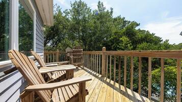 A wooden deck with Adirondack chairs and a table, overlooking a forested area.