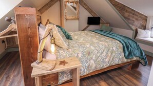 A bedroom with a sloped ceiling, a bed with a floral bedspread, a wooden headboard, and a small table with a light fixture. - Driftwood (Bridlington)