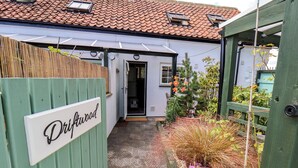 A gated entrance to a property named 'Driftwood' with a tiled roof, a wooden fence, and a garden with various plants and flowers. - Driftwood (Bridlington)