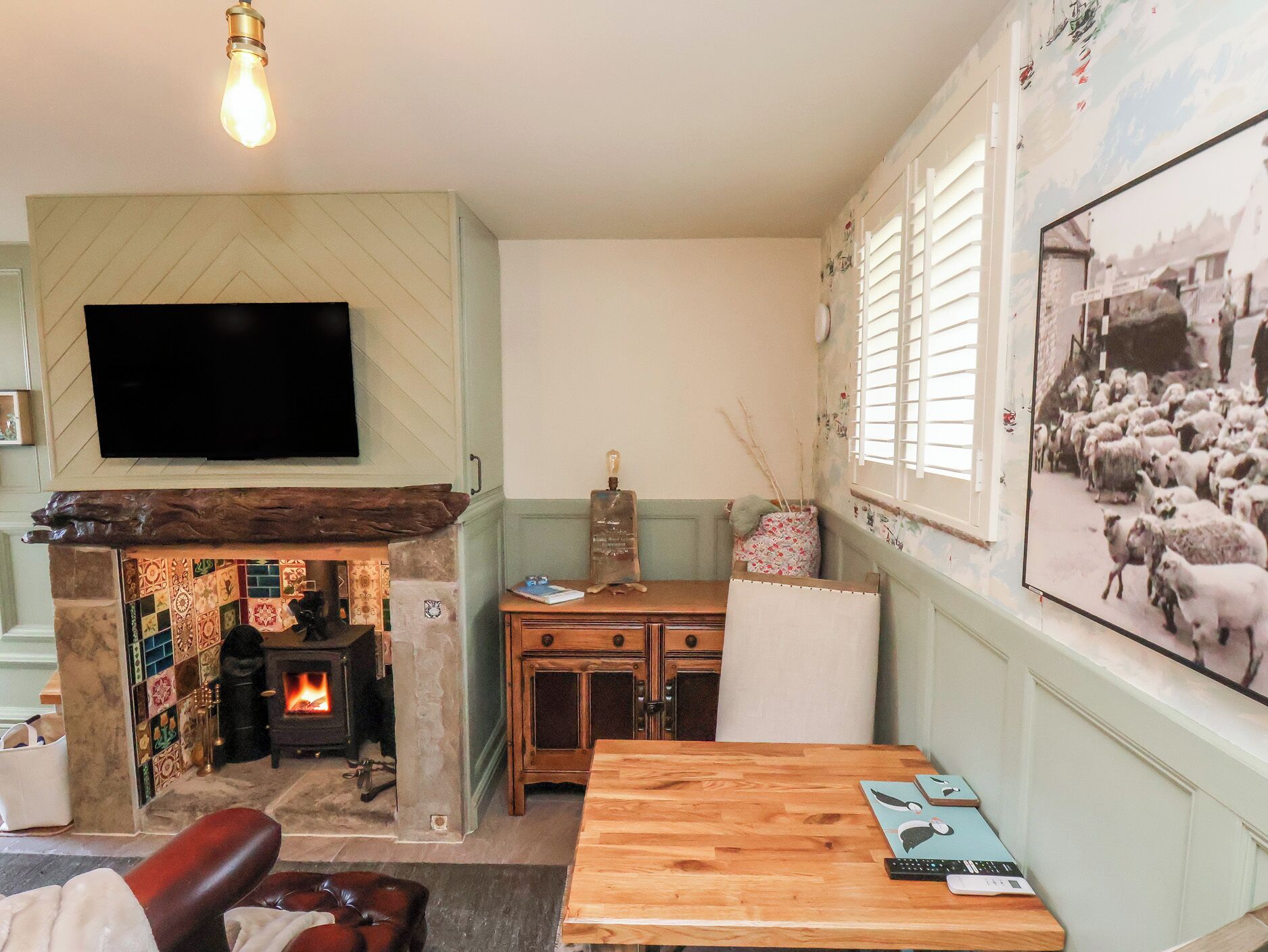 A cozy living room with a fireplace, a television mounted on the wall, and a large framed picture of sheep.