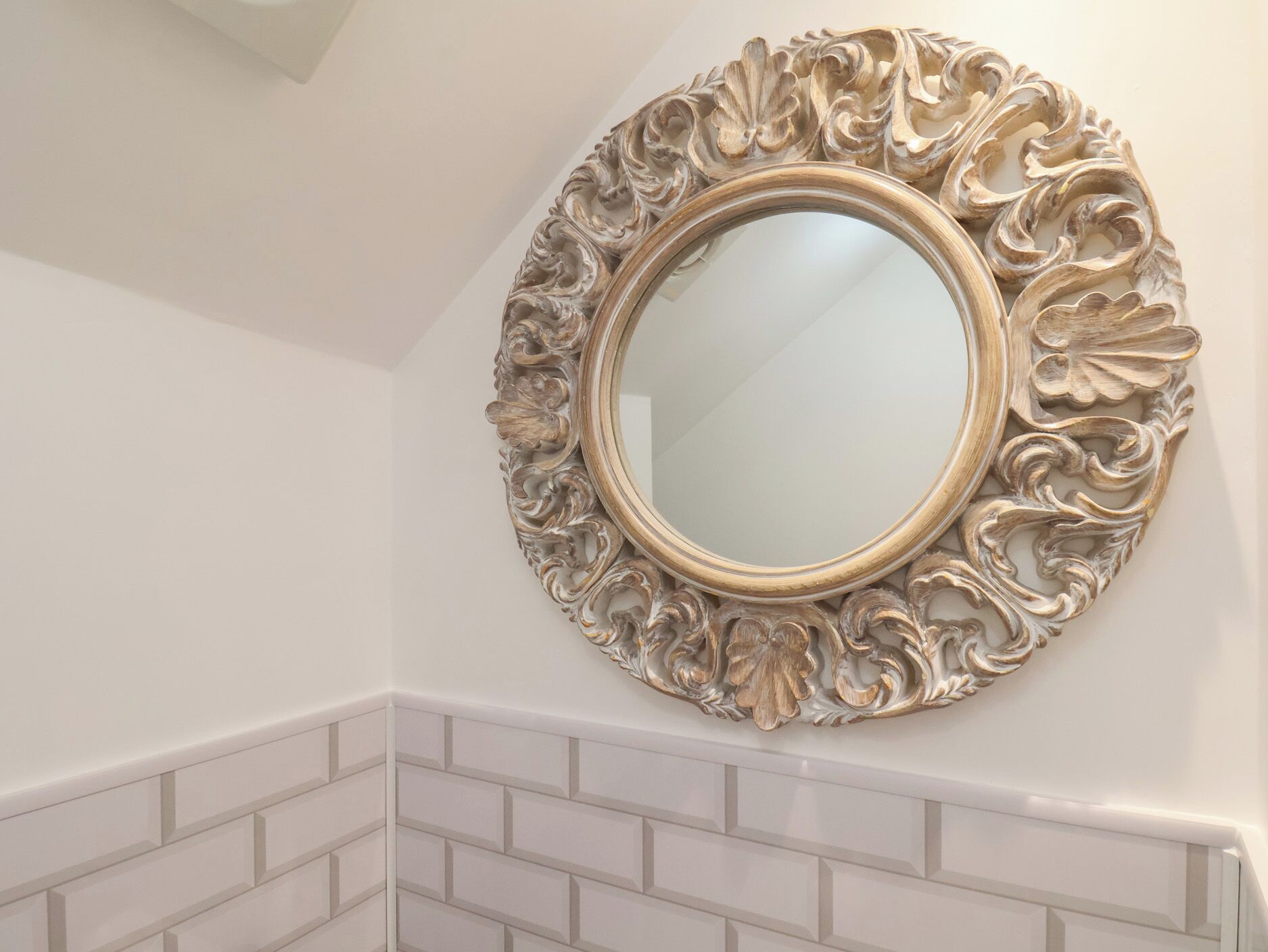 Un baño con un espejo decorativo y paredes cubiertas de azulejos blancos.
