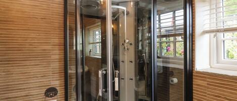 A corner bathroom with a glass enclosure, a toilet, and a window with blinds.