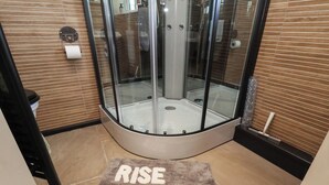 A glass-enclosed shower area with a "RISE & SHINE" mat in the foreground. - Driftwood (Bridlington)