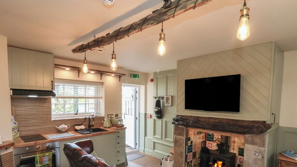 A cozy kitchen with a fireplace, a television mounted above it, and a seating area with a cushioned chair and a bench. - Driftwood (Bridlington)
