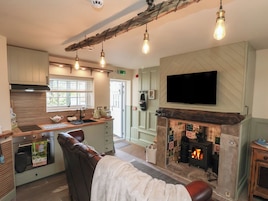 Una cocina acogedora con chimenea, un televisor montado encima y una zona de estar con una silla acolchada y un banco.