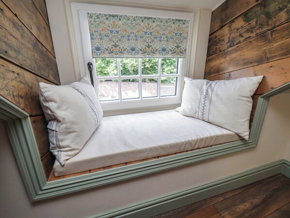 A cozy reading nook with a built-in bench, a window with a floral blind, and wooden paneling. - Driftwood (Bridlington)