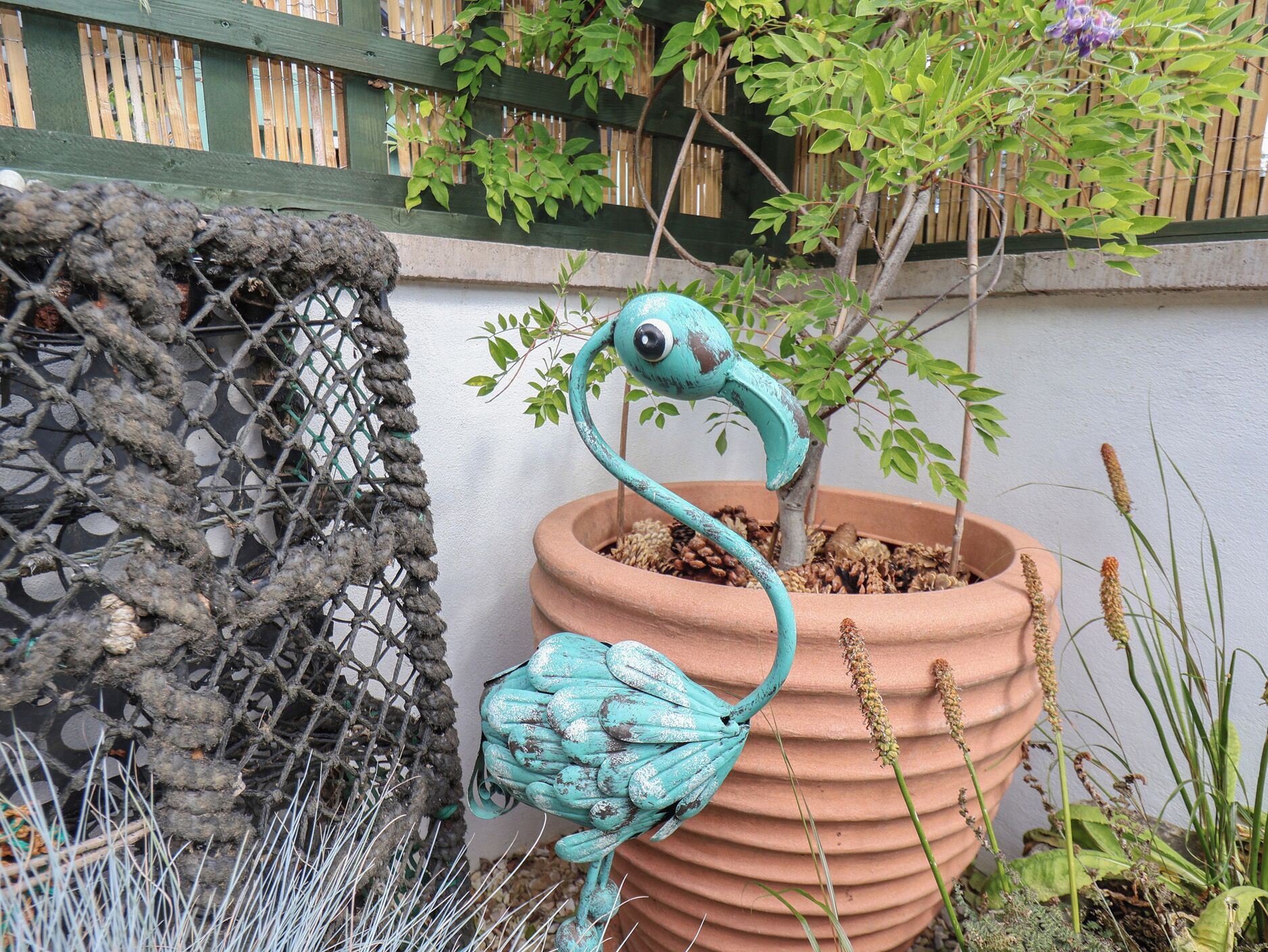 A terracotta pot with a blue bird sculpture and a small tree.