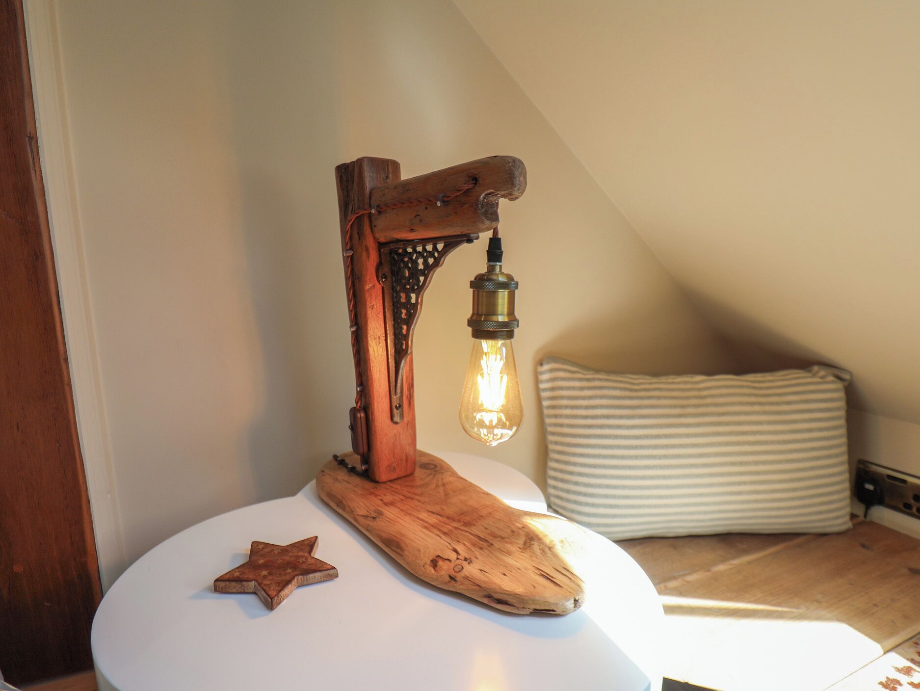 A rustic wooden desk lamp with a star-shaped object on a white surface, a striped pillow, and a slanted ceiling.