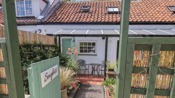 Ein Innenhof mit einem grünen Tor mit der Aufschrift „Seaglass“, einem Ziegeldach und einer kleinen Terrasse mit Stühlen und Tisch.