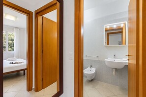 A hotel room with a bed, a bedside table, a window with curtains, and a bathroom with a sink, bidet, and mirror. - Seaview & Pool Retreat Il Poggio (Andora)