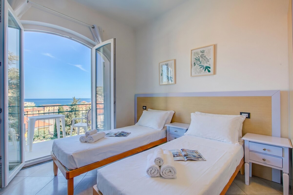 A hotel room with two beds, a balcony with a view, and a small table with a chair.