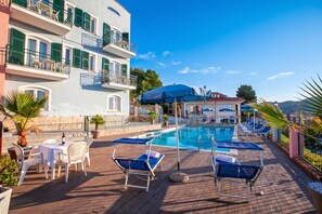 A poolside area with lounge chairs, a table with chairs, and a building with balconies. - Seaview & Pool Retreat Il Poggio (Andora)