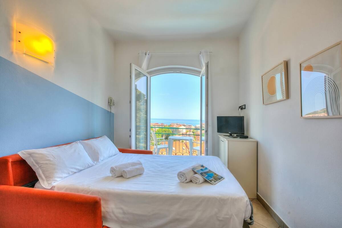 A hotel room with a bed, a TV, a balcony with a view, and a desk.