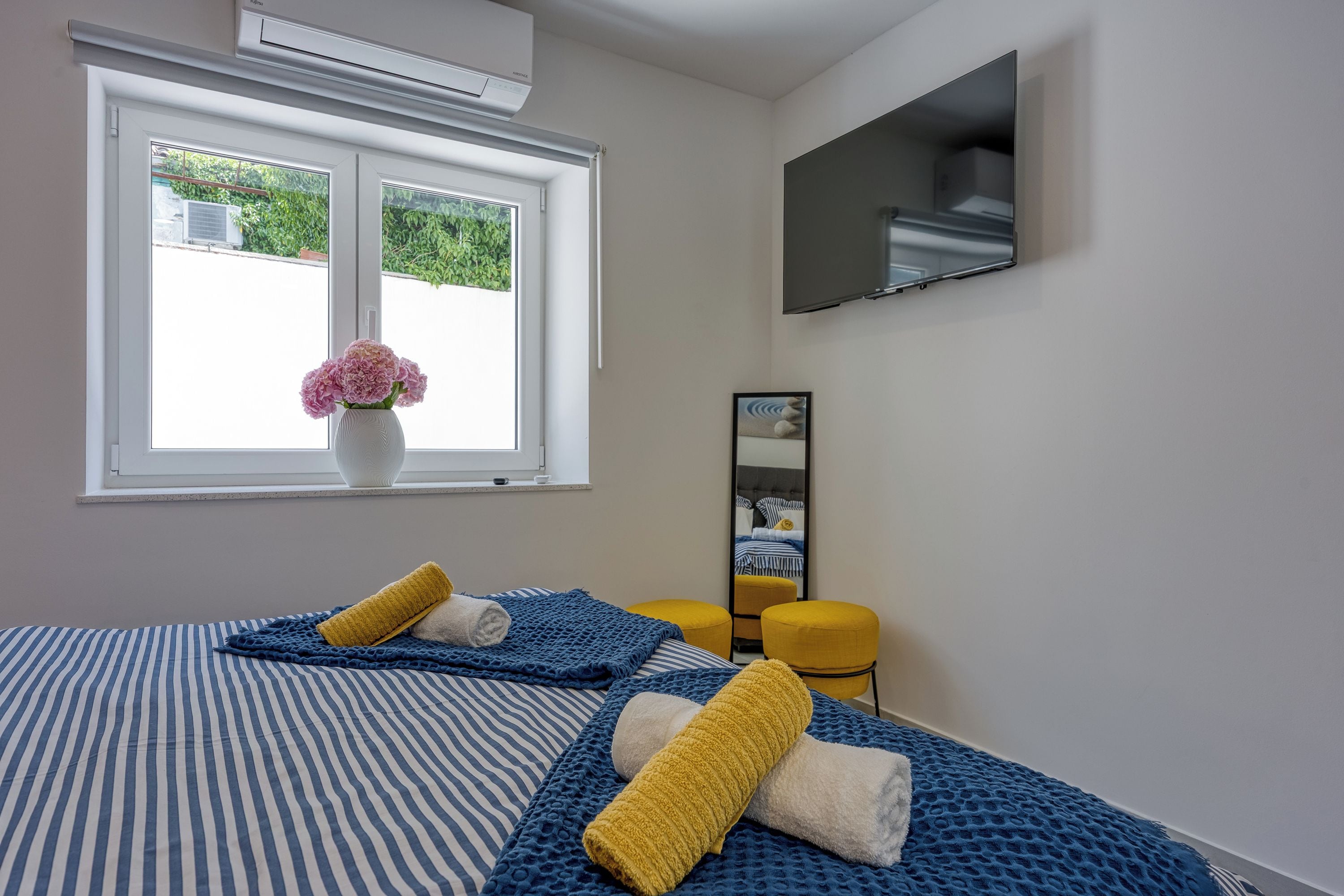 A hotel room with a bed, a window with a view, a flat-screen TV, and a mirror.