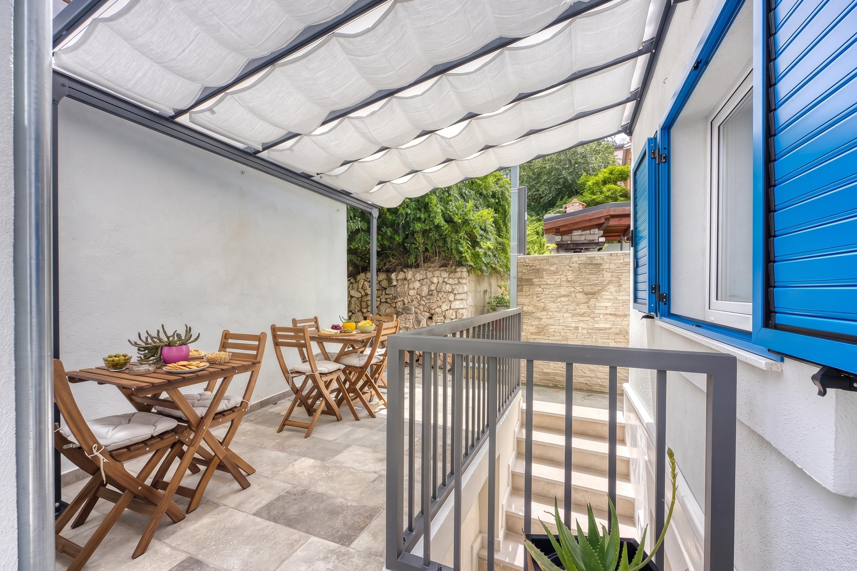 Ein überdachter Patio-Bereich mit Esstisch, Holzstühlen und einer Steinsäule im Hintergrund.