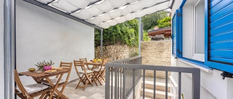 A covered patio area with a table set for dining, wooden chairs, and a stone wall in the background.