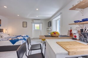 Habitación de hotel moderna con cama, escritorio, silla, mesa de comedor y kitchenette con frutero.