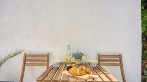 Ein Holztisch mit zwei Stühlen, einer Flasche, einem Einmachglas, einem Croissant und einem Glas Saft.